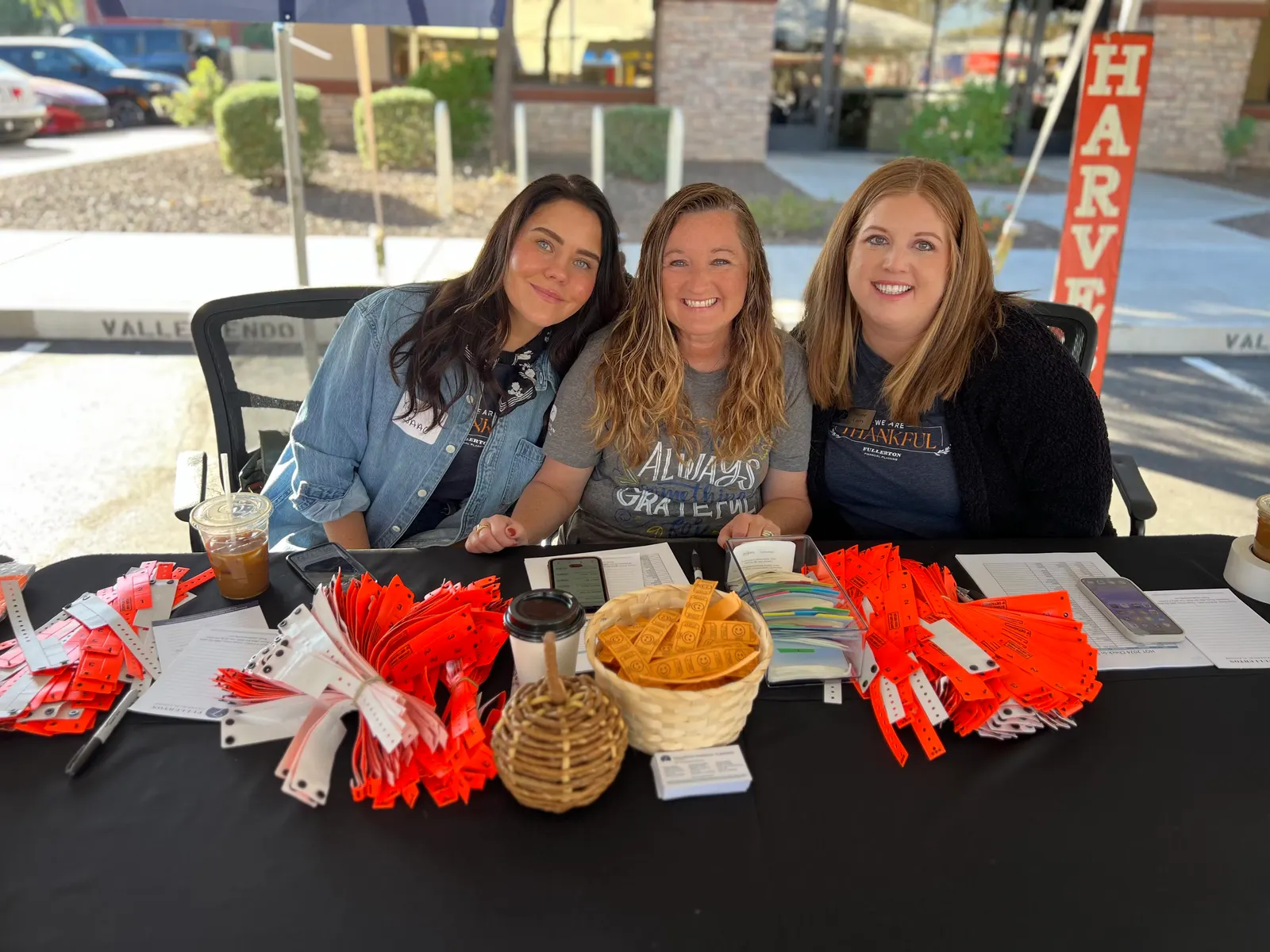 Three people at a registration table beside a Harvest of Thanks sign