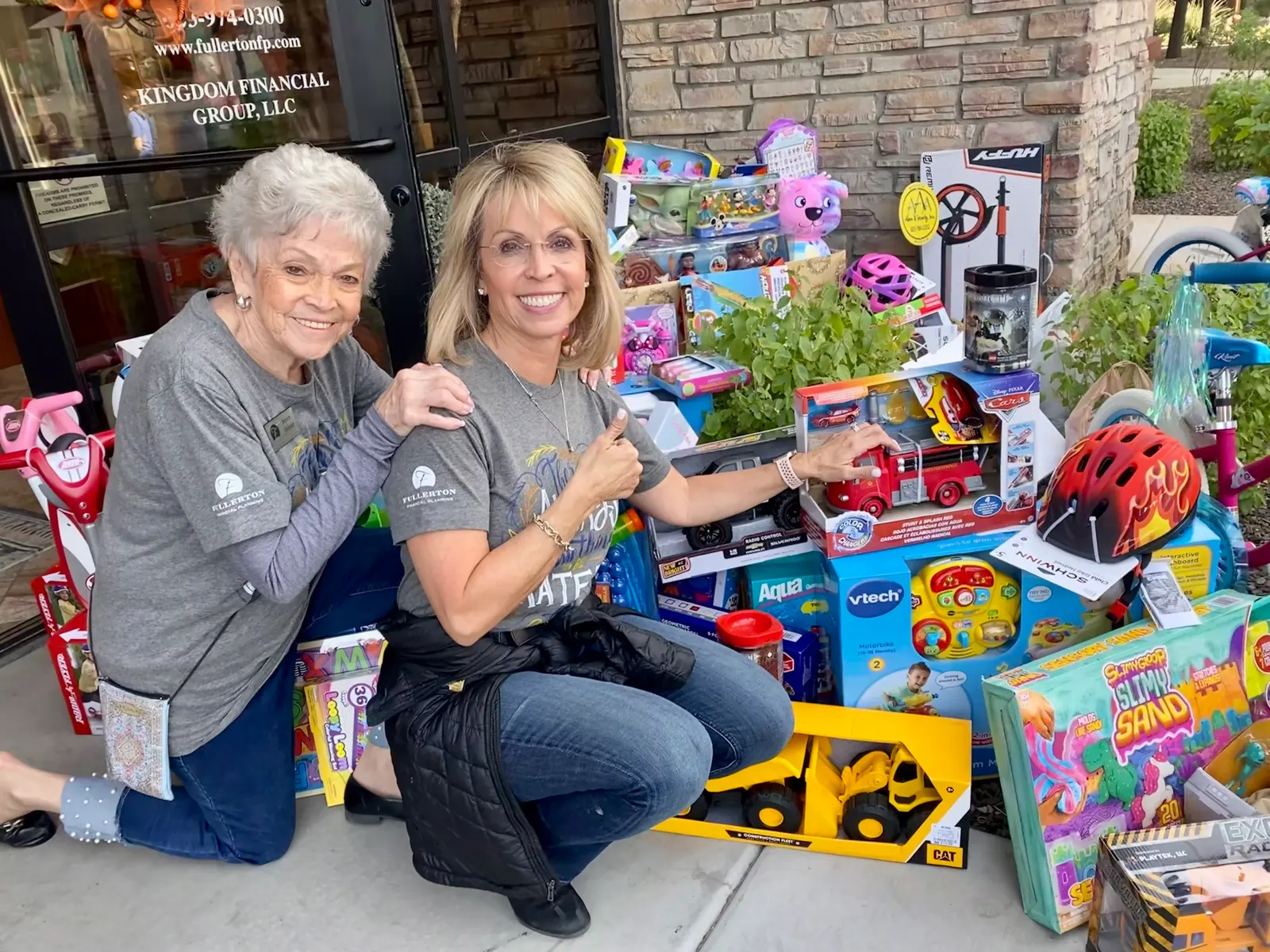 Two people kneeling beside a display of donated toys and bikes