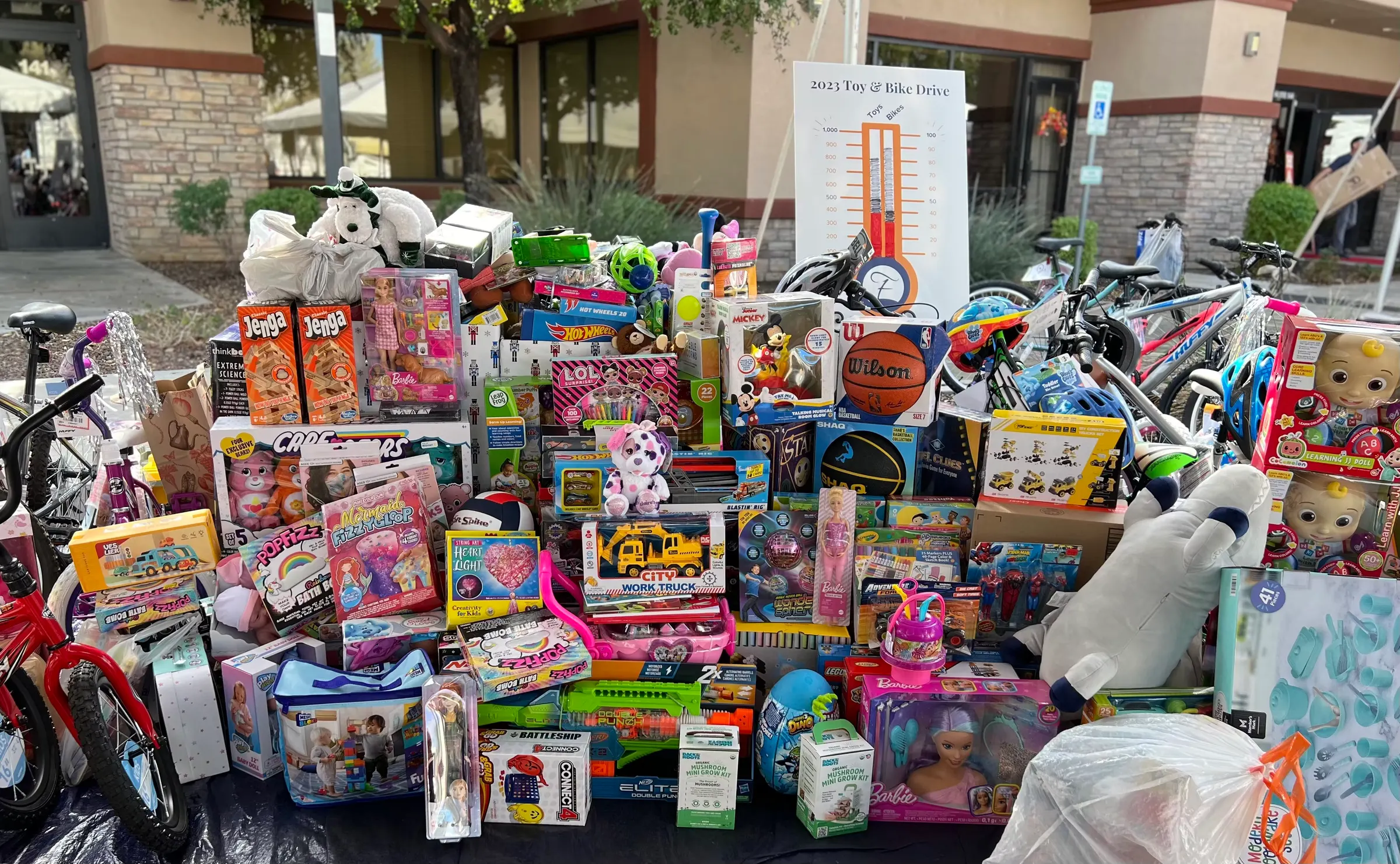 Toys and bikes laid out on a table beneath the Toy & Bike Drive goal thermometer